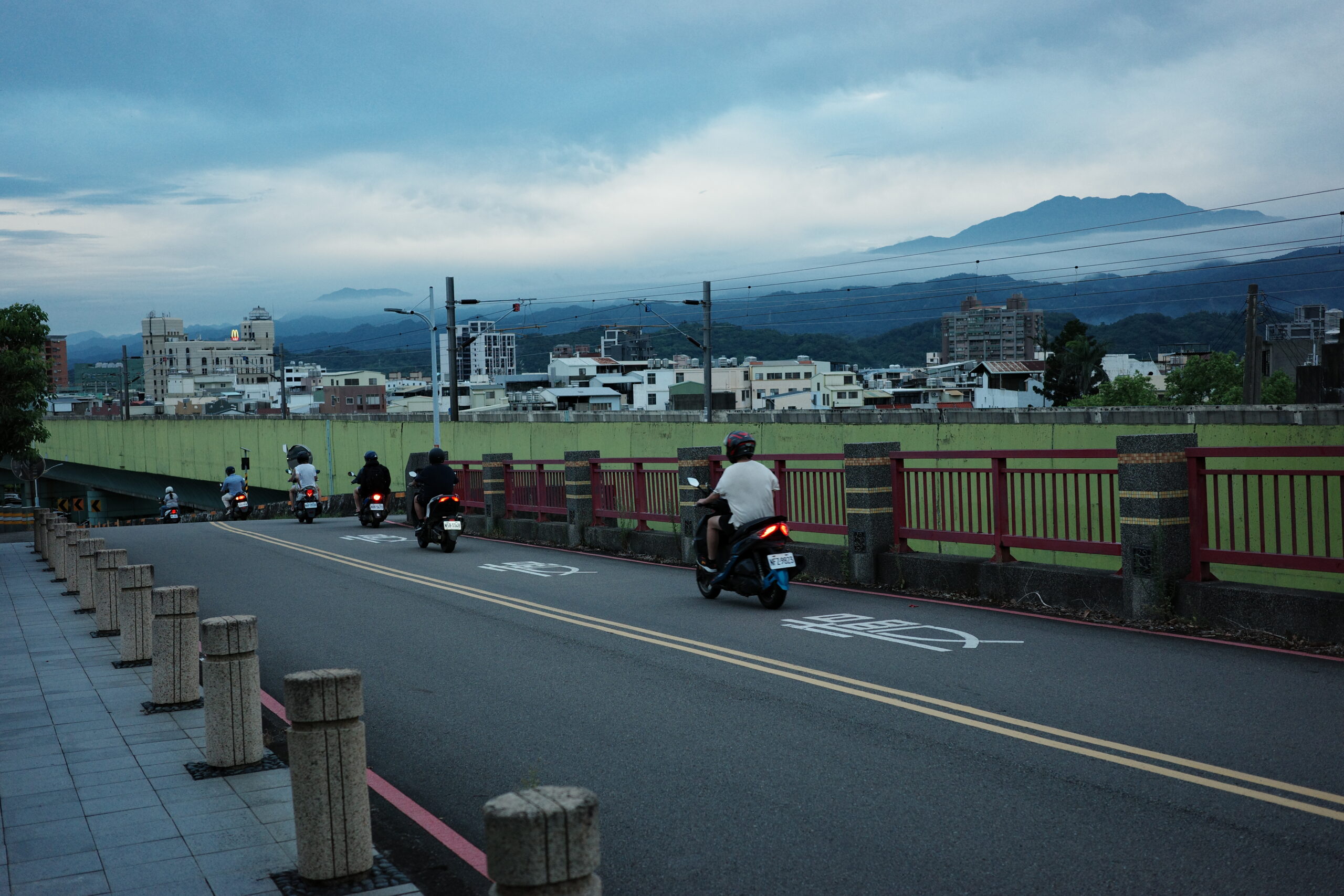 Scooters crossing a bridge at twilight, evening air settling in.