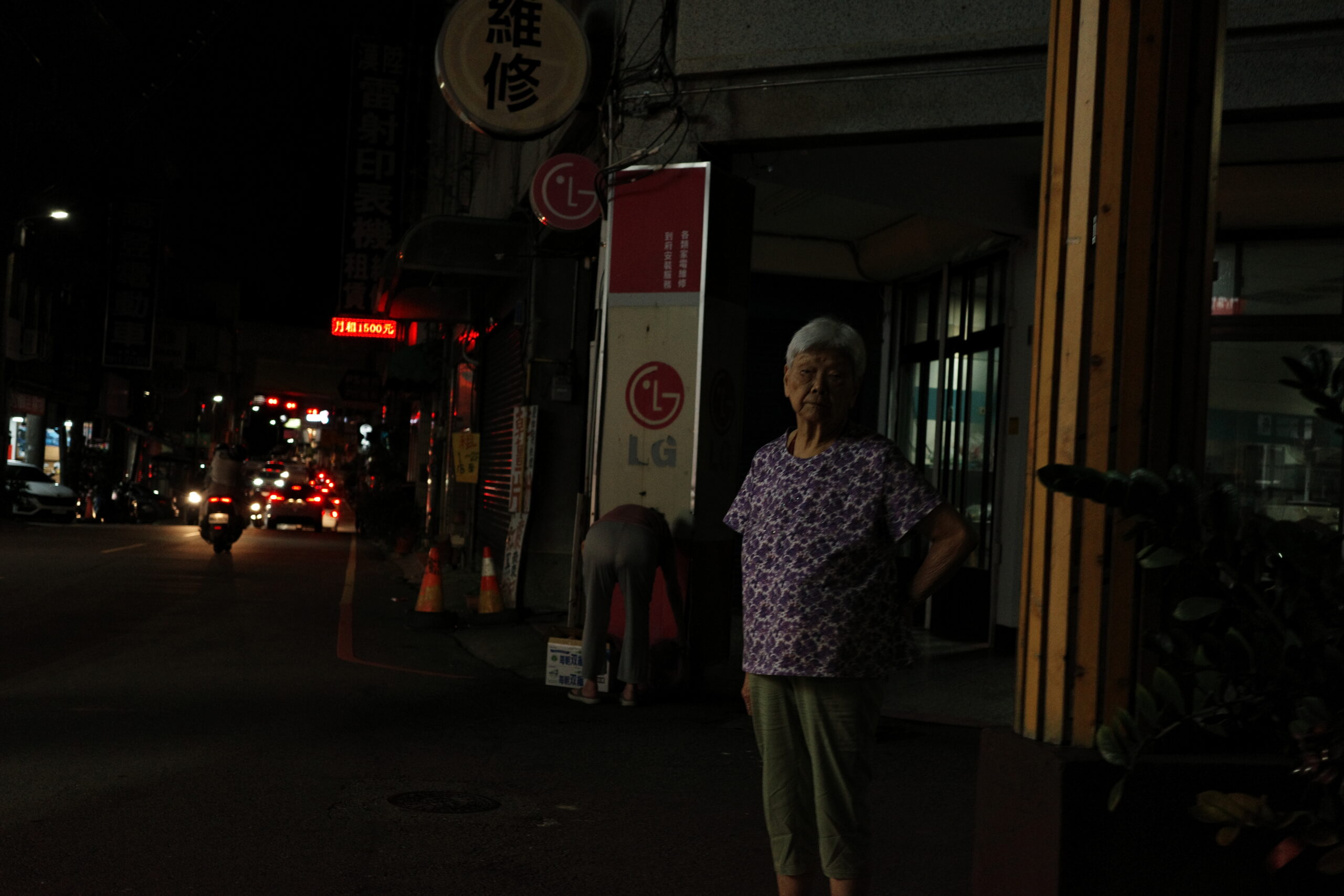 A lone figure standing near a dimly lit corner under warm streetlight.